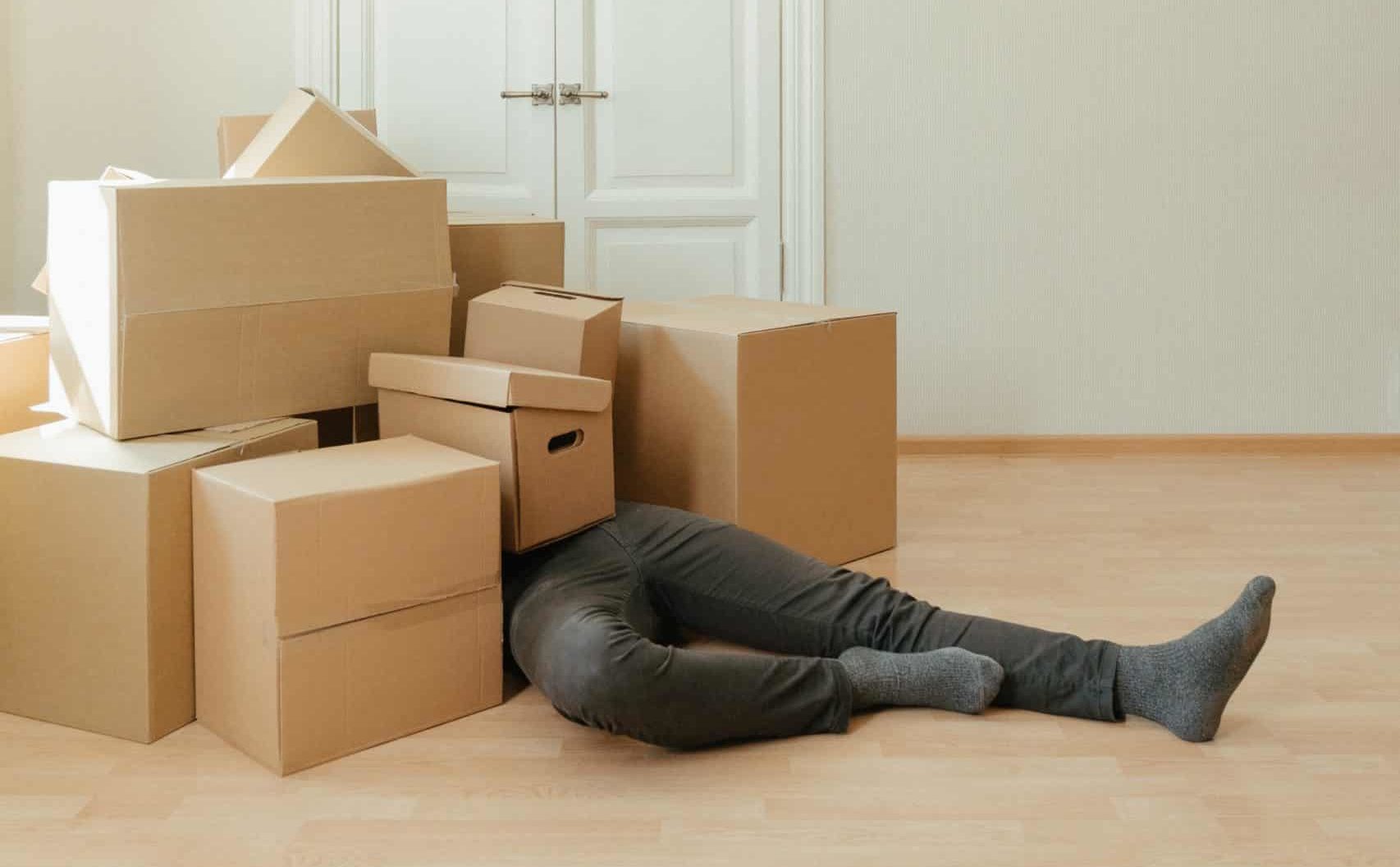 A man lays under a pile of cardboard moving boxes.