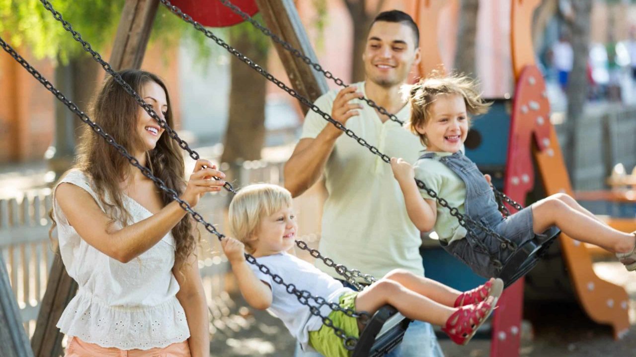 Parents push their children on a swing set in a public playground in Minneapolis, one of the best places to raise a family.